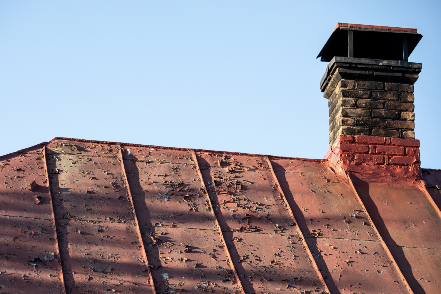 Old painted metal roof. Peeling paint and an old brick chimney