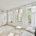 a living room with white walls and wood flooring, two large windows in the wall is covered with sheer curtains