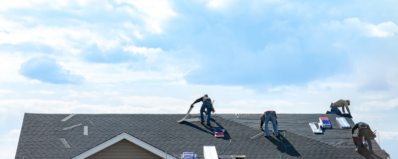 4 construction workers fixing roof against clouds blue sky, install shingles at the top of the house. Renovate, improvement, build home exterior by professional teamwork. Safety and protection concept