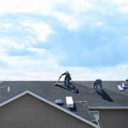 4 construction workers fixing roof against clouds blue sky, install shingles at the top of the house. Renovate, improvement, build home exterior by professional teamwork. Safety and protection concept