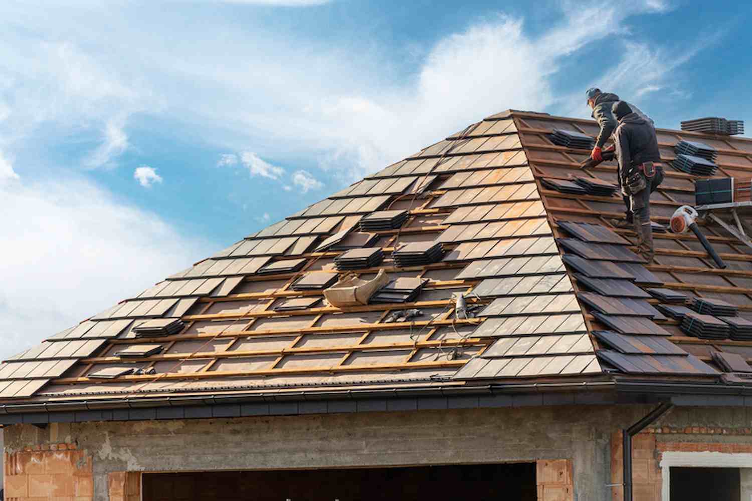 process of building, roofer workers installing grey metal tile on top of roof with wooden frame outdoors on blue sky background