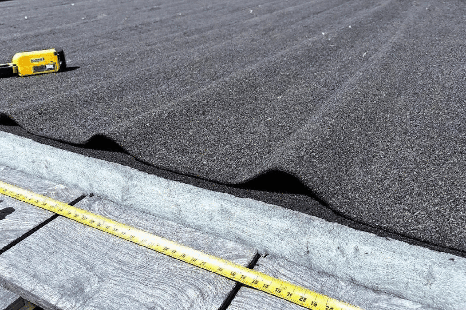 The image shows a close-up view of a synthetic underlayment installation, highlighting the correct placement of fasteners on a roof deck.